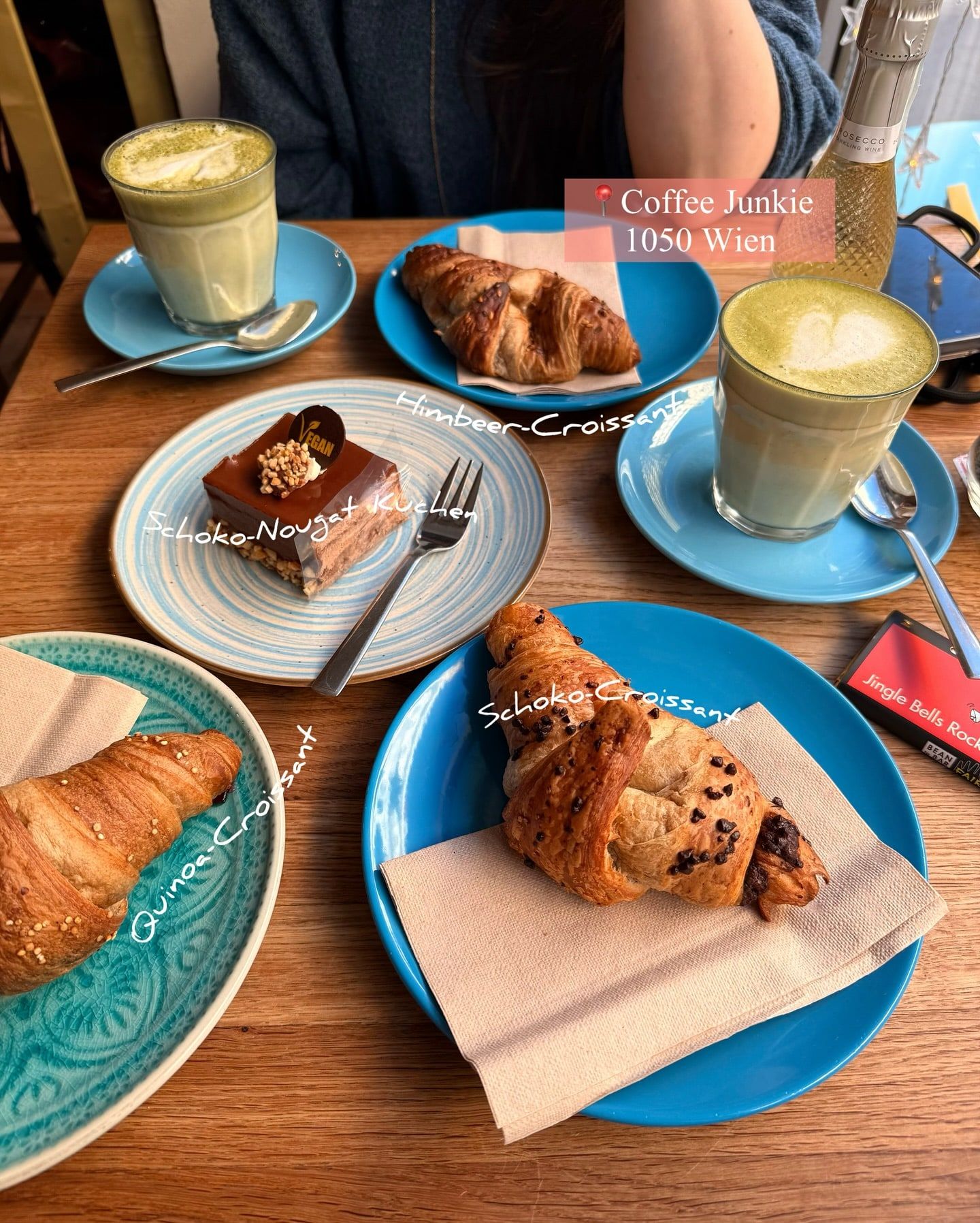 Croissants and a chocolate nougat cake on blue plates next to two matcha lattes, labelled in German