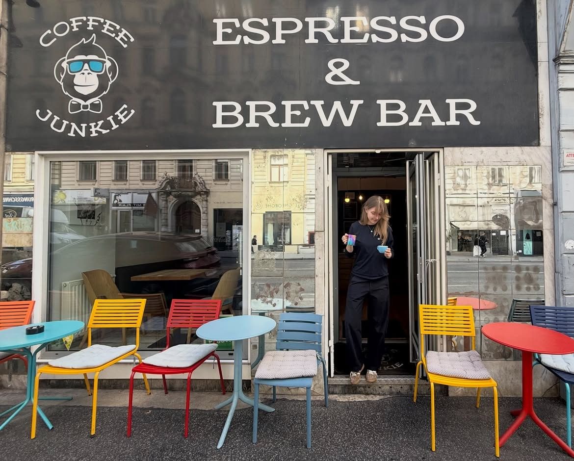 The Coffee Junkie shopfront: black sign with the sunglasses-wearing monkey logo, 'Espresso & Brew Bar', colourful chairs outside